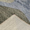 Close-up of multi-colored abstract rug with curved green, gray, and blue shapes and beige edge binding.