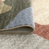 Multi-colored abstract patterned rug with muted earth tones and soft blue accents, folded corner shows low pile texture.