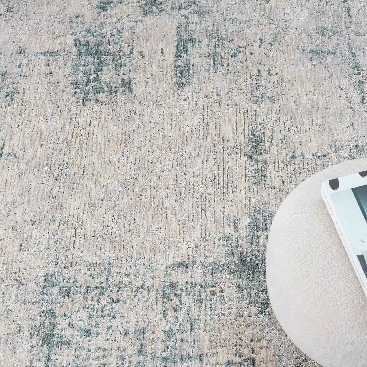 Textured area rug with a neutral color palette and a round ottoman corner.