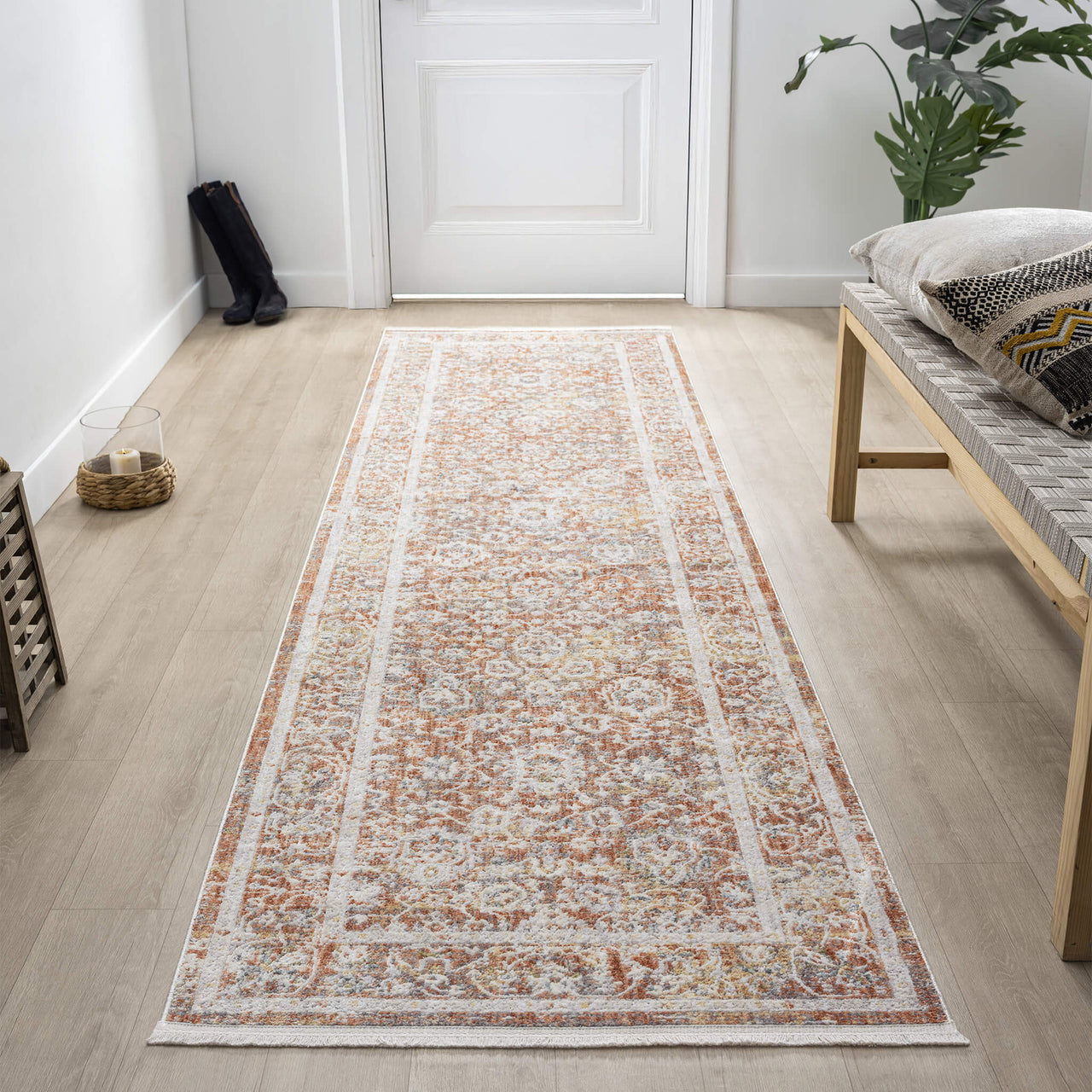 Long rectangular rug with a pattern on a wooden floor in a room with a bench and plant.
