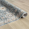 Blue transitional rug with intricate floral pattern and subtle multicolor accents rolled on light wood floor.