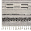 Grey rug with layered geometric patterns and textured pile, featuring tassels on one edge.
