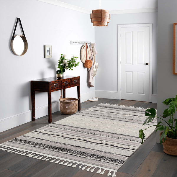 Grey geometric patterned rug with textured pile and fringed edges on hardwood floor.