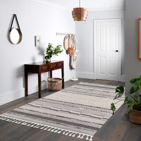 Grey geometric patterned rug with textured pile and fringed edges on hardwood floor.