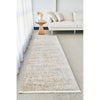 Long beige rug on a light gray floor in a living room setting with a white sofa and wooden side table.