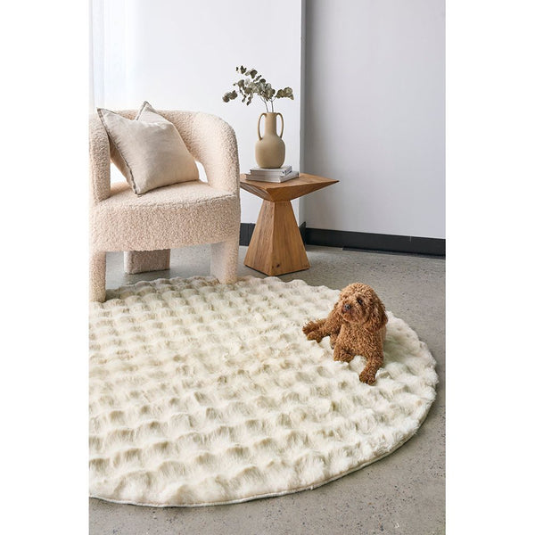 Round natural cream rug with textured bubble pattern on polished concrete floor.