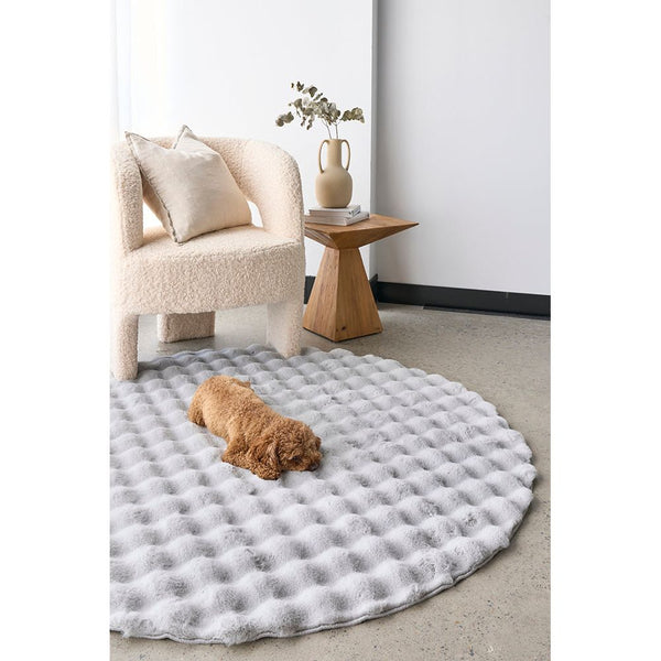 Round silver grey textured rug with raised bubble pattern under small dog in a modern living space.