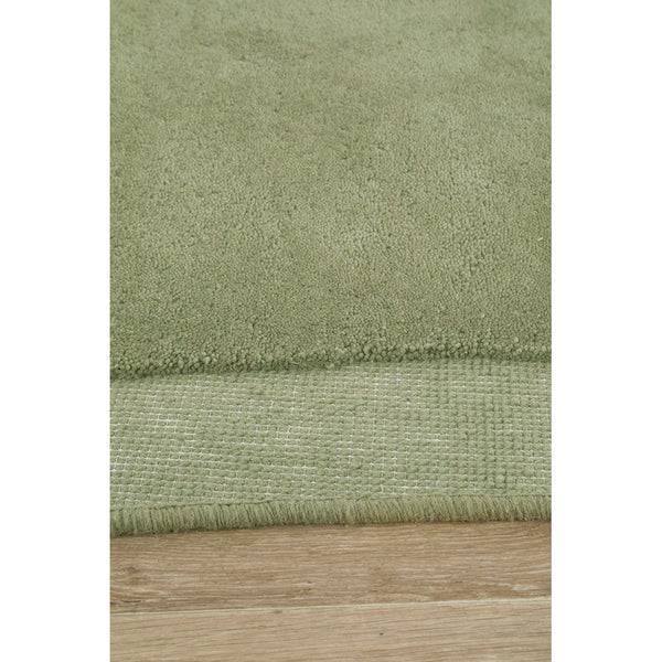 Soft green curved wool rug with a thick hand-tufted texture on light wood floor.