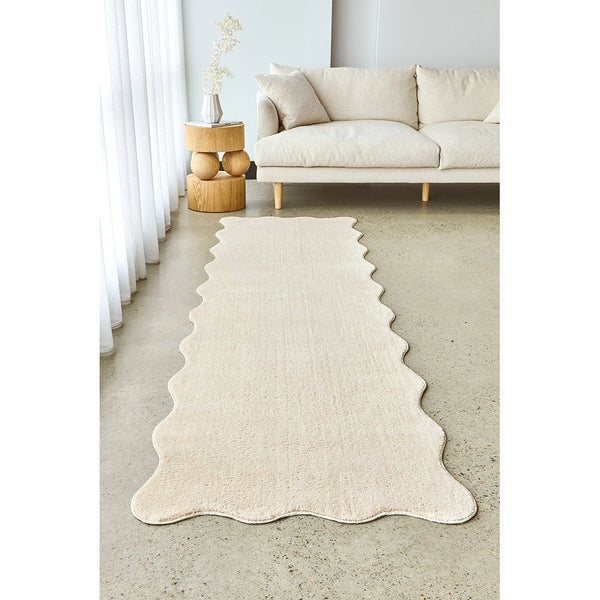 Beige modern runner rug with scalloped edges on light floor in a bright living room.