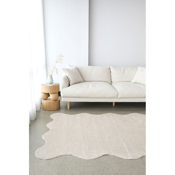 Beige modern rug with irregular wavy edges on light floor by cream sofa.
