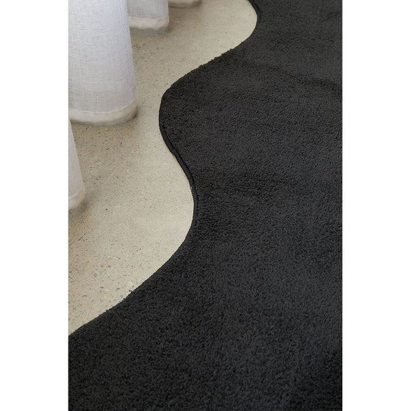 Black modern rug with curved edge detail on light concrete floor.