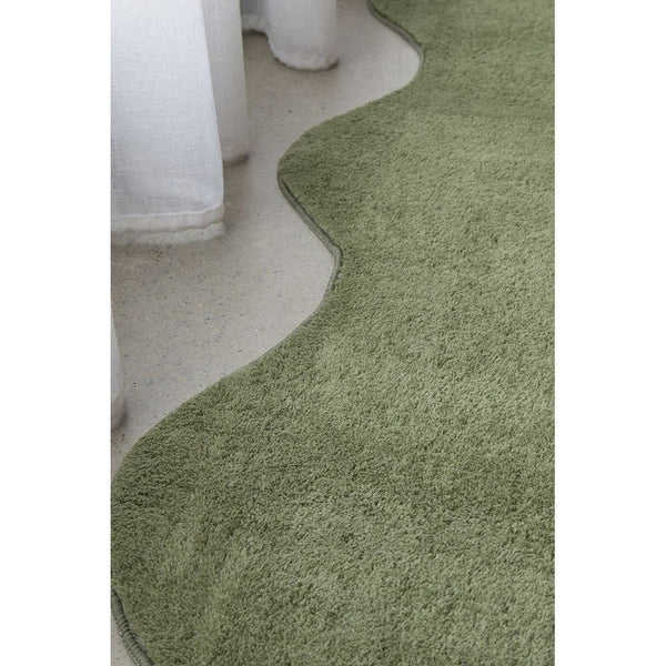 Green machine washable runner rug with soft texture and scalloped edges on a light floor.