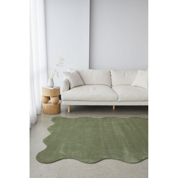 Green irregular-shaped modern rug with soft texture placed in front of beige sofa.