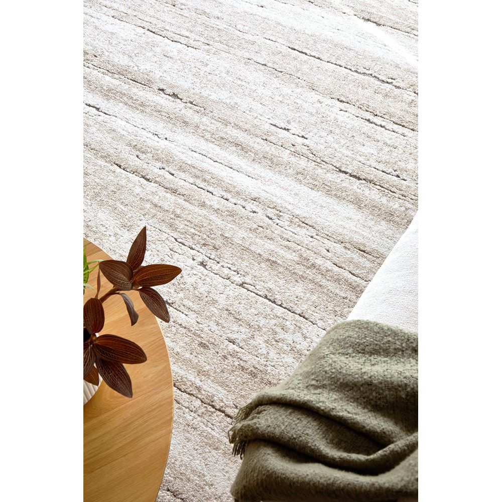 Close-up of a textured beige rug with a plant and folded green fabric on a wooden surface.