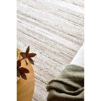 Close-up of a textured beige rug with a plant and folded green fabric on a wooden surface.