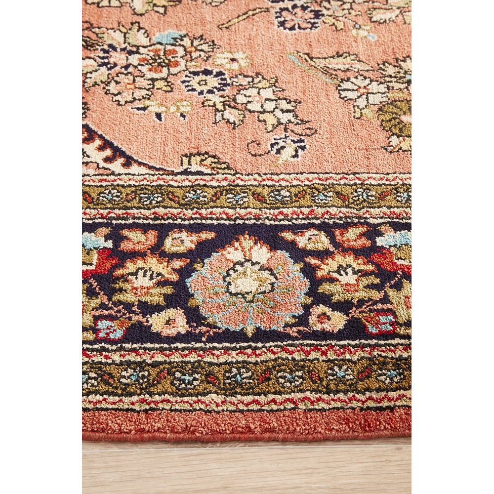 Close-up of a patterned hand knotted Persian silk rug with floral designs on a wooden floor.