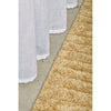 Close-up of a textured gold rug and white curtain on a neutral background