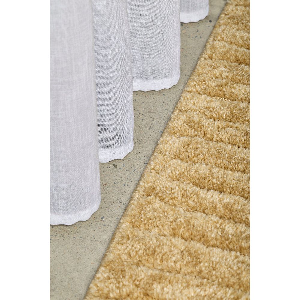 Close-up of a textured beige rug and white curtain on a neutral background