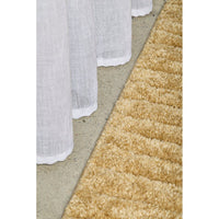 Close-up of a textured beige rug and white curtain on a neutral background