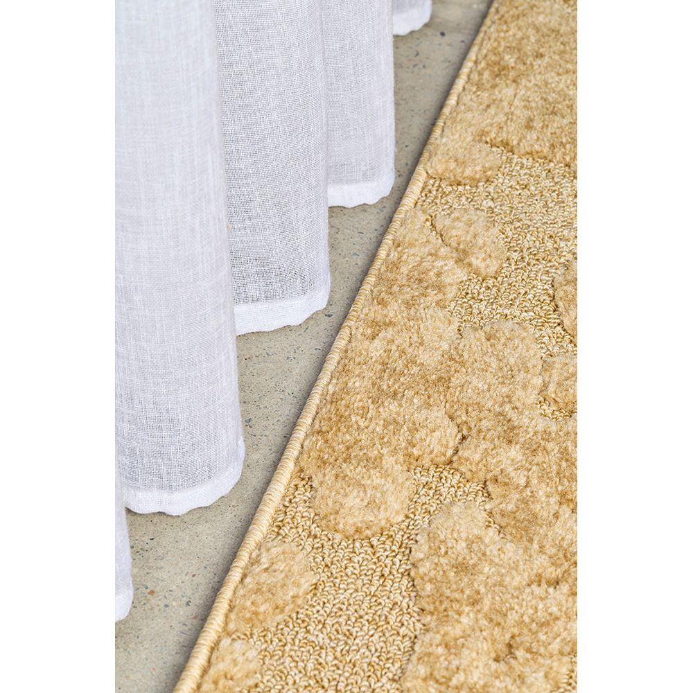 Close-up of a textured gold rug corner on a concrete floor.