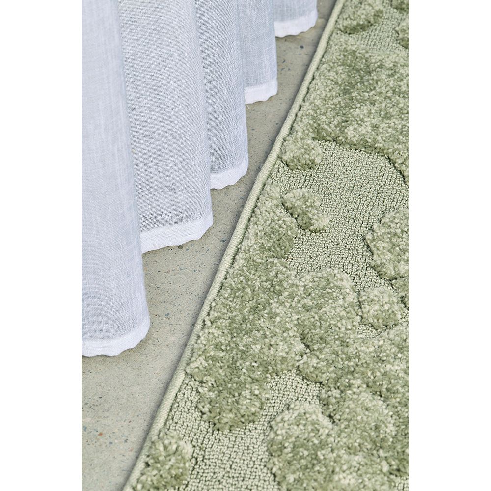 Close-up of a textured green runner rug and a white curtain on a neutral background