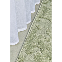Close-up of a textured green runner rug and a white curtain on a neutral background