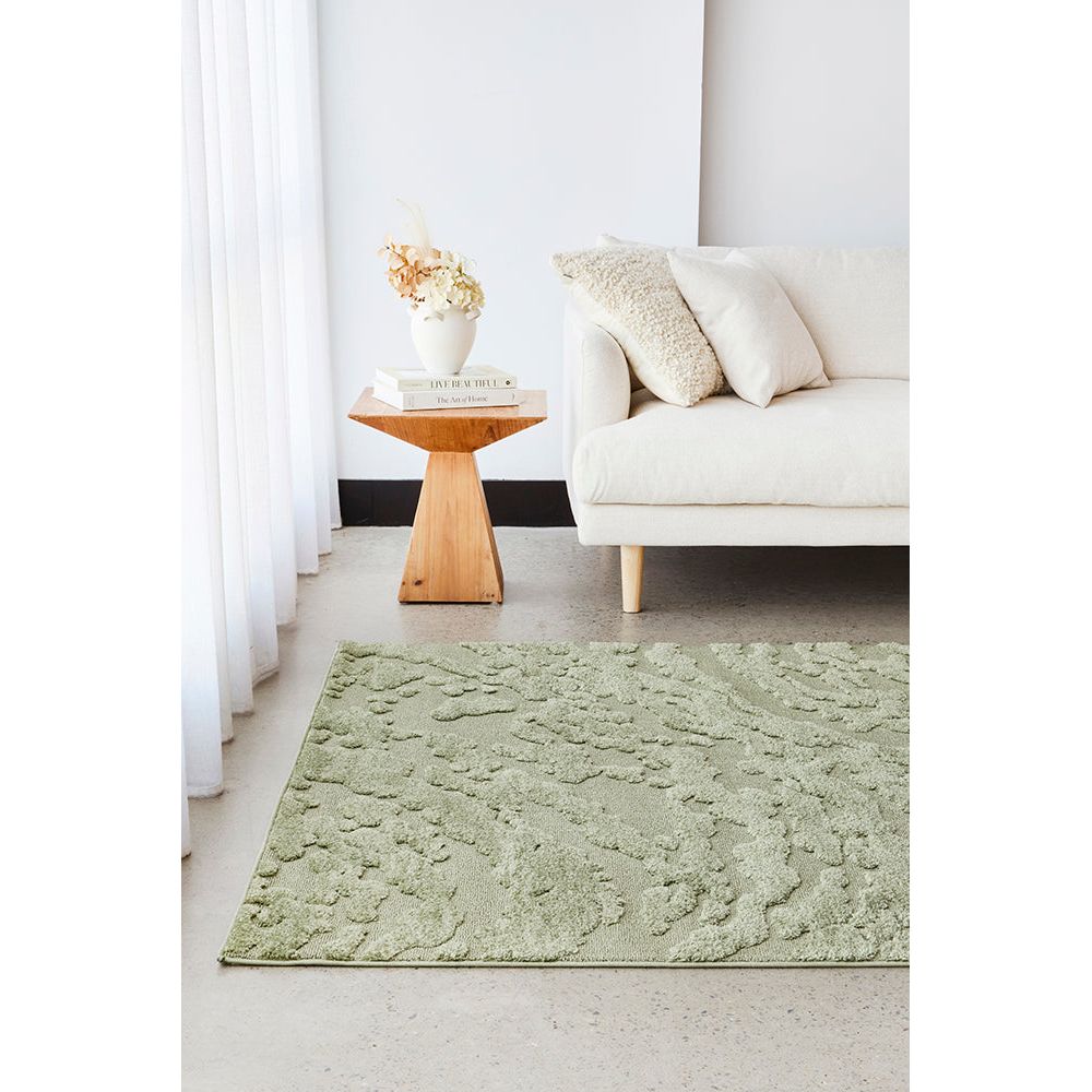 Green rug on a light gray floor with a white sofa and wooden side table in the background.