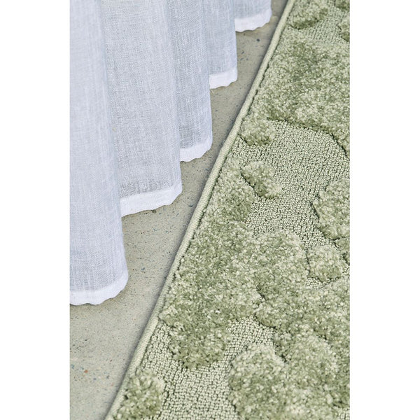 Close-up of green textured rug with modern geometric pattern next to white sheer curtains.