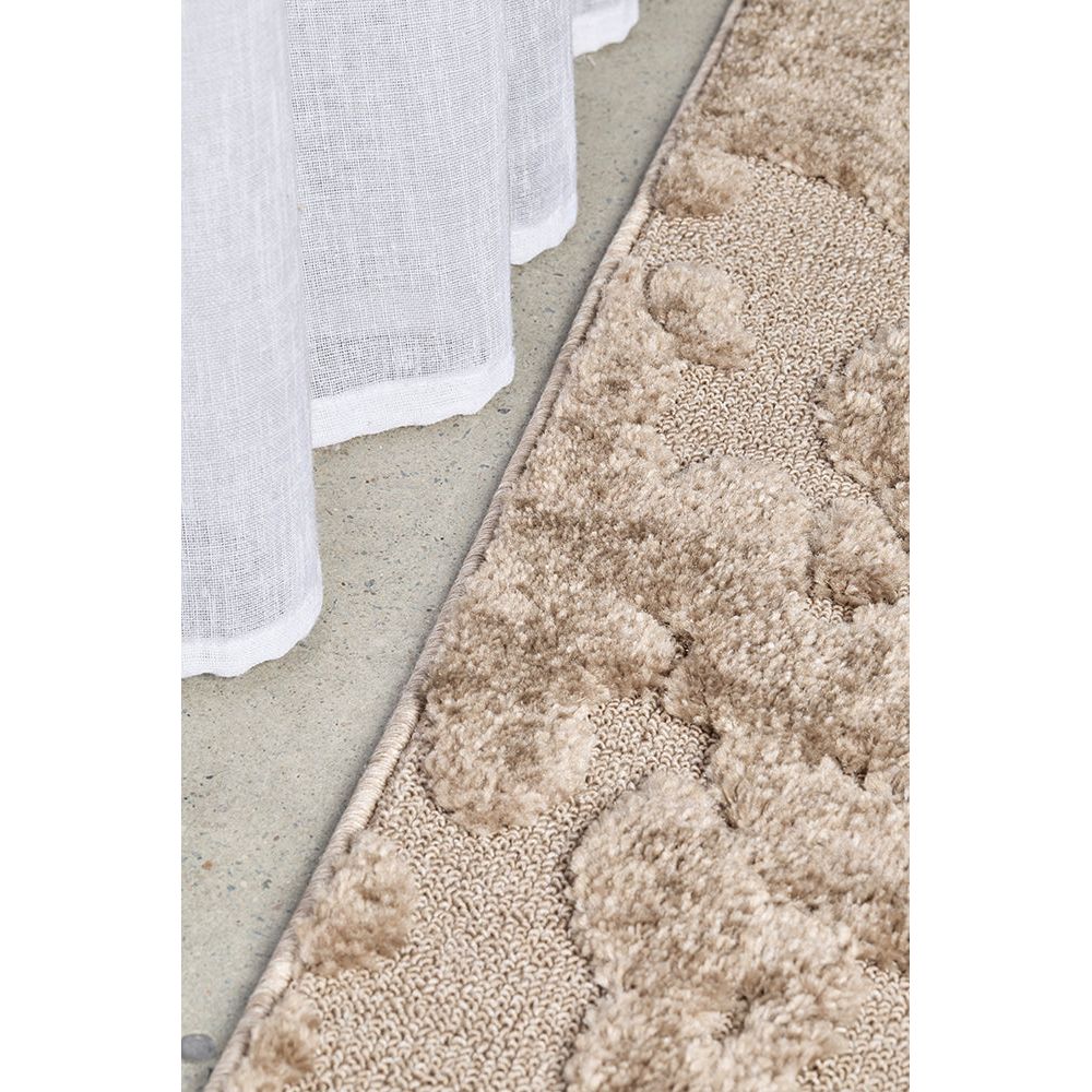 Close-up of a textured beige rug on a concrete floor with white curtains.