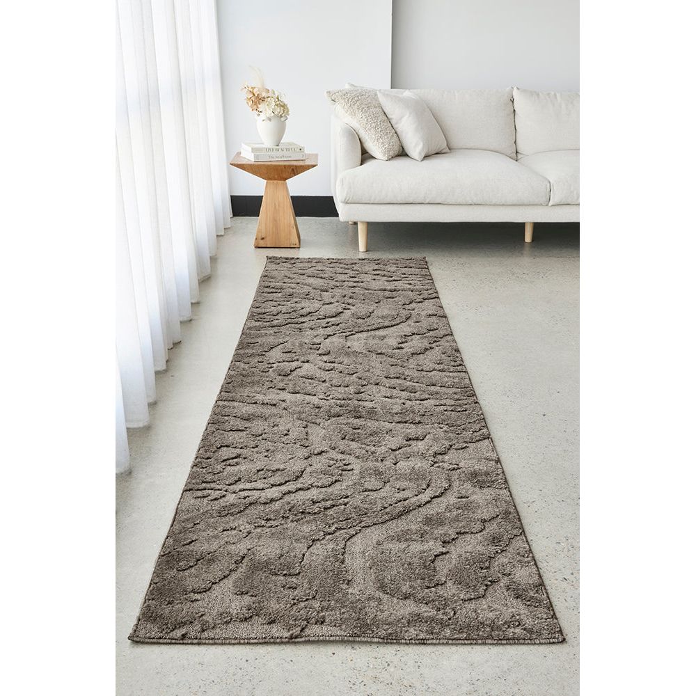 Long, textured brown mocha rug on a light gray floor in a living room setting with a white sofa and small table.