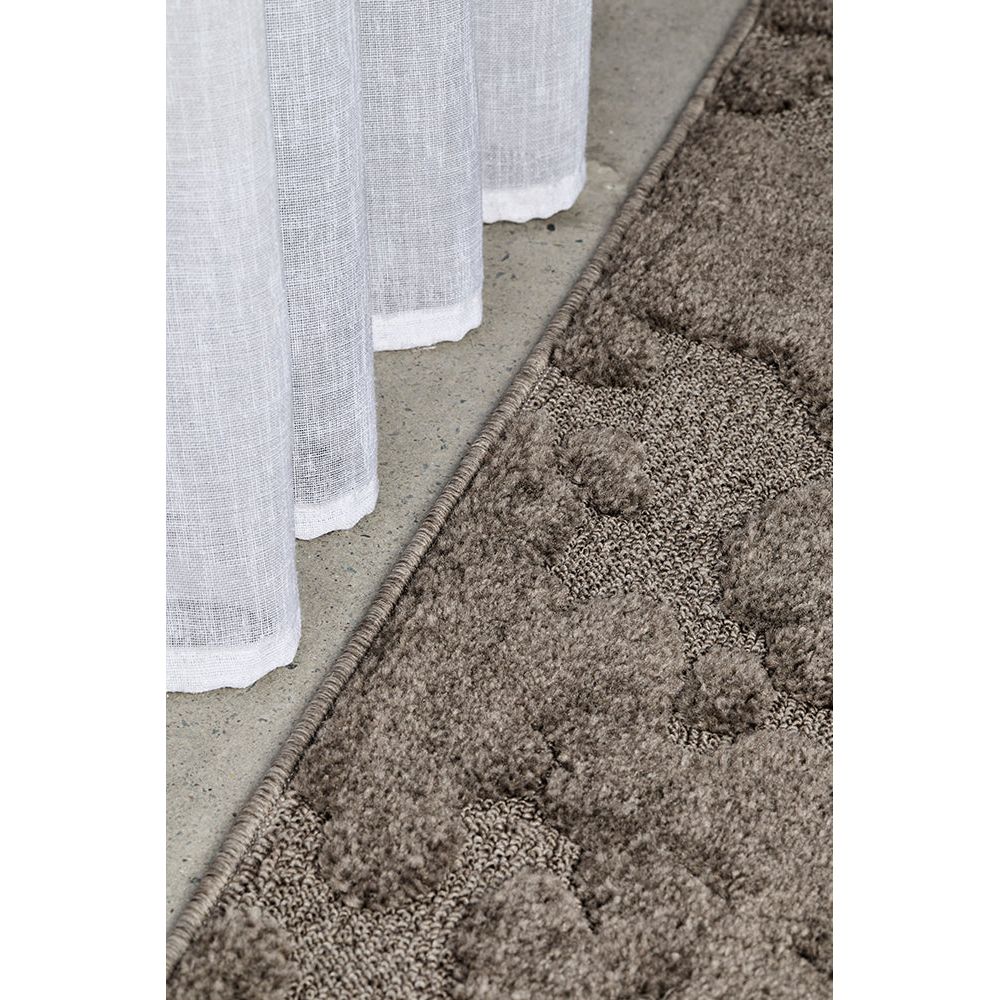 Close-up of a textured brown rug with a white curtain in the background.