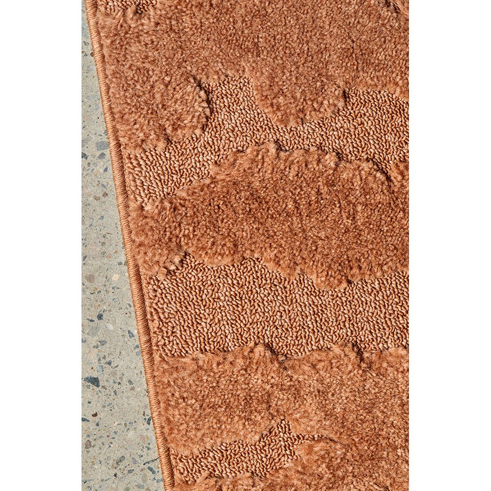 Close-up of a textured rust coloured rug on a concrete floor.