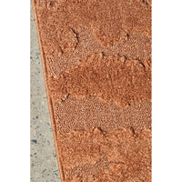 Close-up of a textured rust coloured rug on a concrete floor.