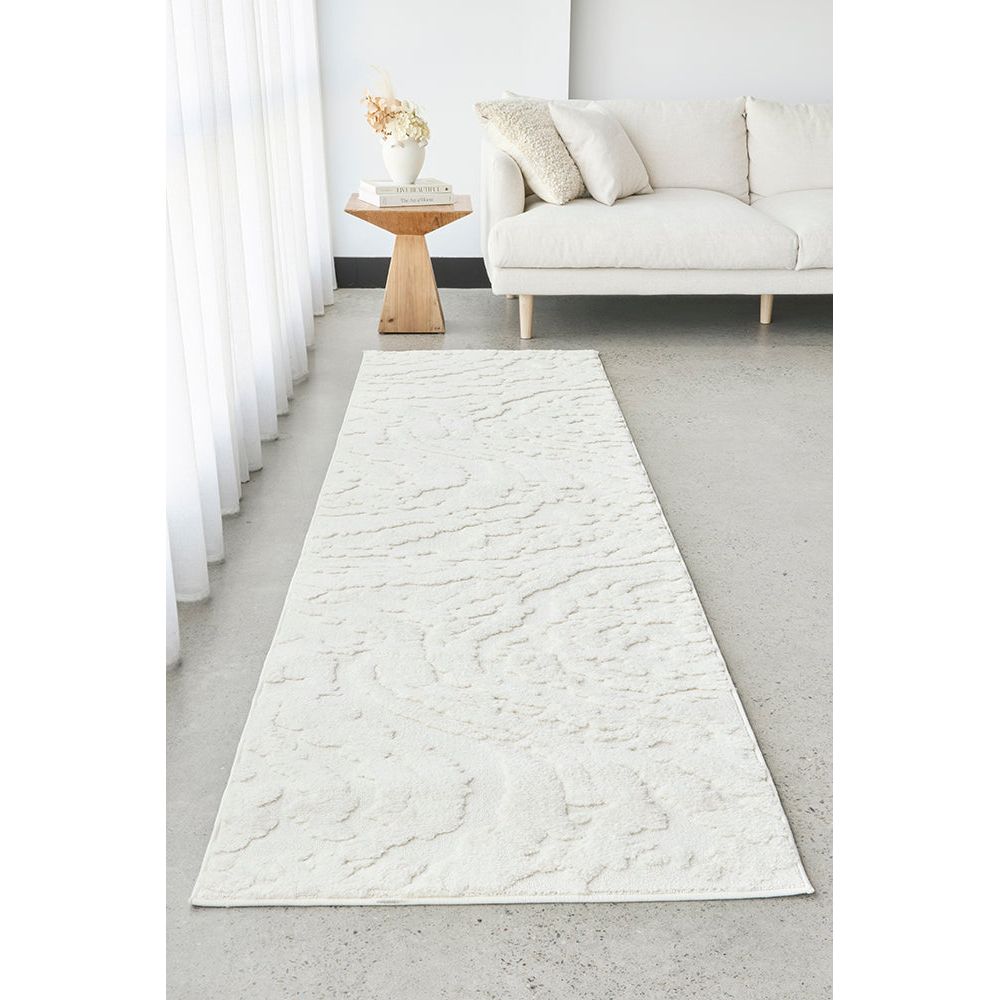 White textured runner rug in a living room setting with a white sofa and wooden side table.