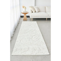 White textured runner rug in a living room setting with a white sofa and wooden side table.