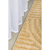 Close-up of a textured gold rug on a concrete floor with white curtains.