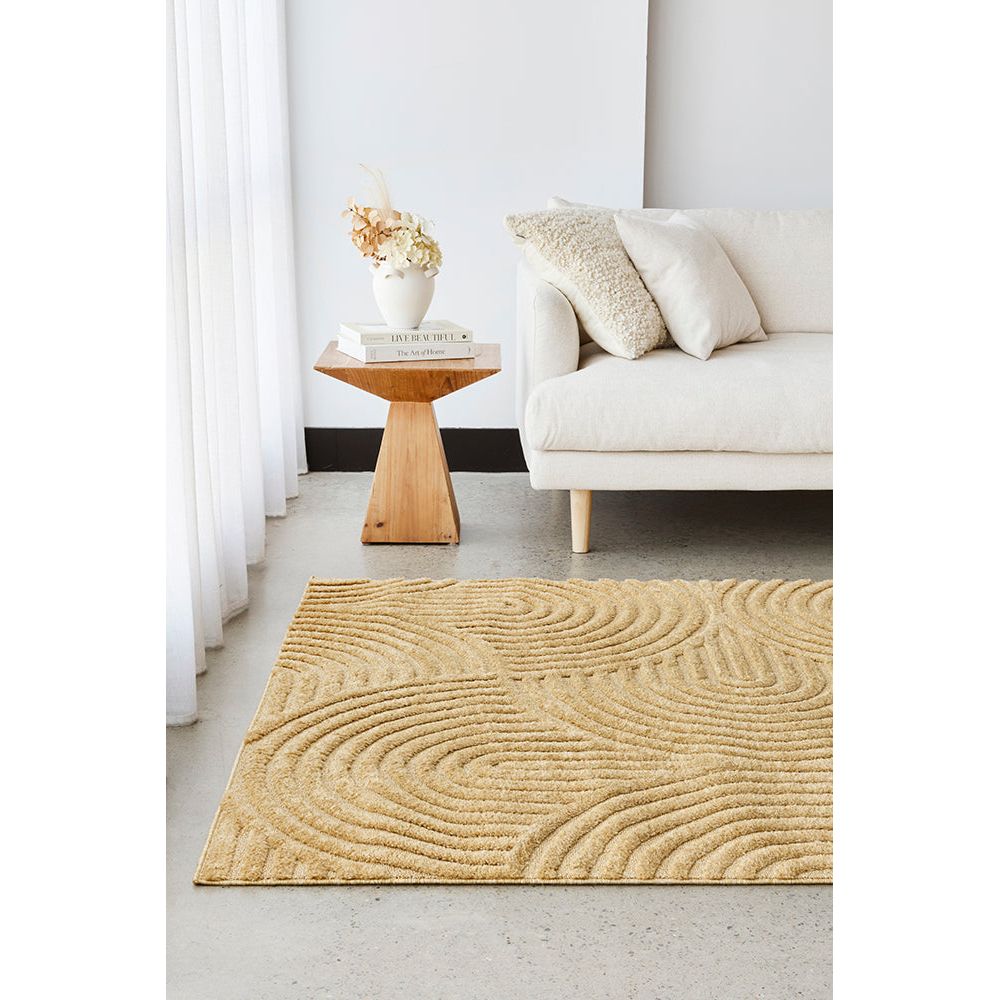 Gold coloured textured rug in a living room with a white sofa and wooden side table.