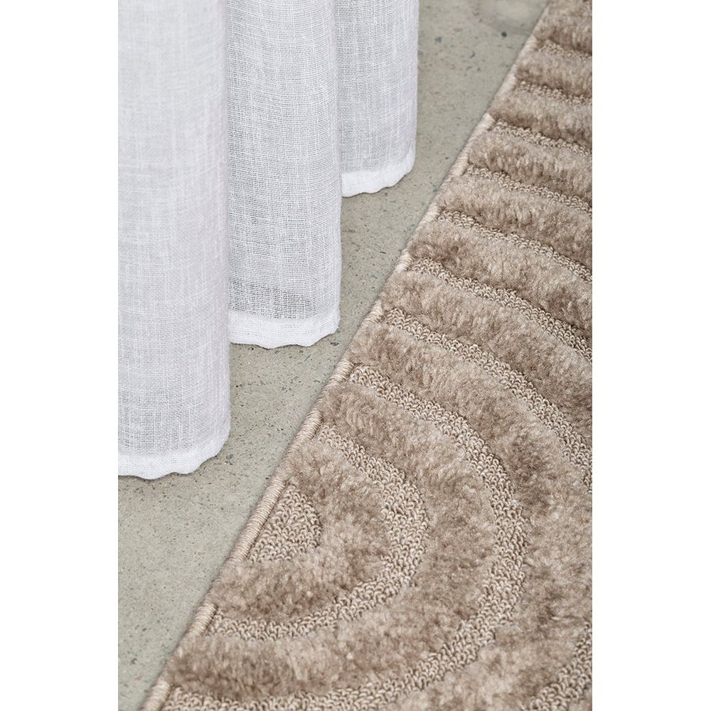 Close-up of a textured beige runner rug on a concrete floor with a white curtain in the background.