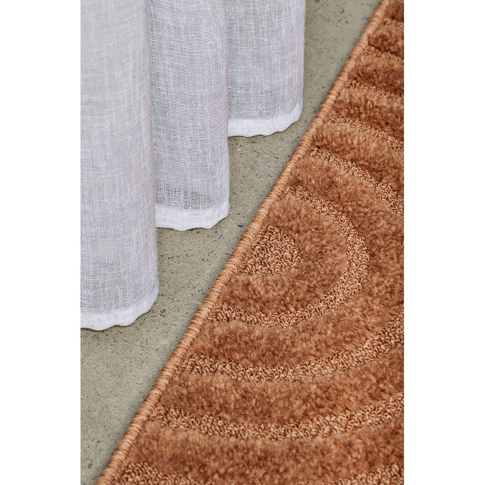 Rust textured rug on a concrete floor with a white curtain partially visible.