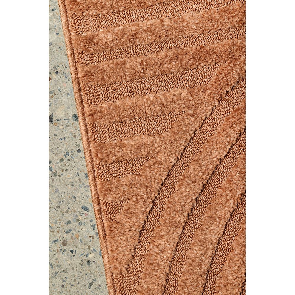 Close-up of a textured rust rug on a concrete floor.