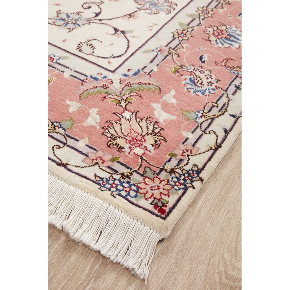 Close-up of a floral patterned rug with tassels on a wooden floor