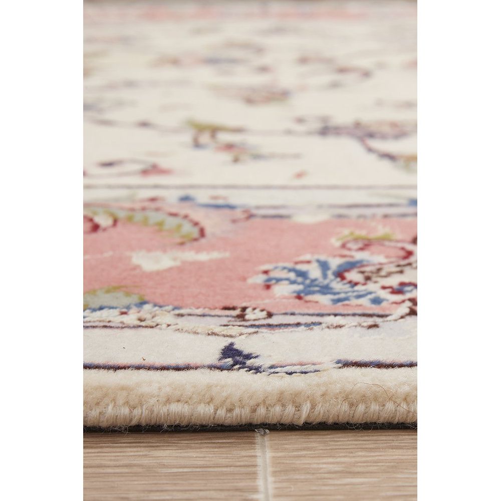 Close-up of a patterned rug with pink and beige colors on a wooden floor.