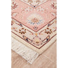 Close-up of a pink and beige floral patterned Persian wool rug with tassels on a wooden floor.
