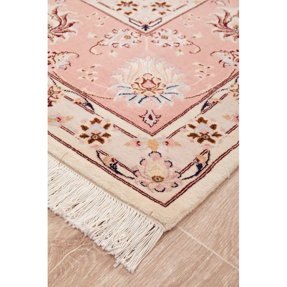 Close-up of a pink and beige floral patterned Persian wool rug with tassels on a wooden floor.