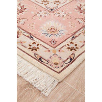 Close-up of a pink and beige floral patterned Persian wool rug with tassels on a wooden floor.