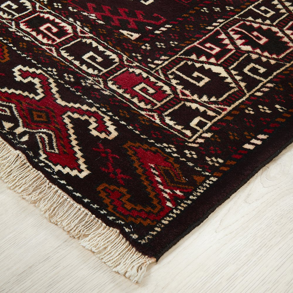 Close-up of a patterned Persian rug with red, brown, and beige colors on a light wooden floor.