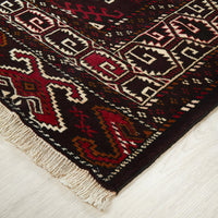 Close-up of a patterned Persian rug with red, brown, and beige colors on a light wooden floor.