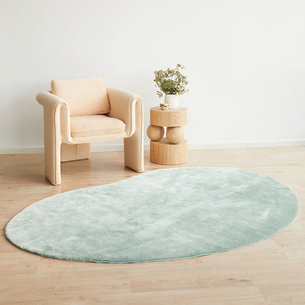 Oval pale green soft rug with plush texture on light wood floor.