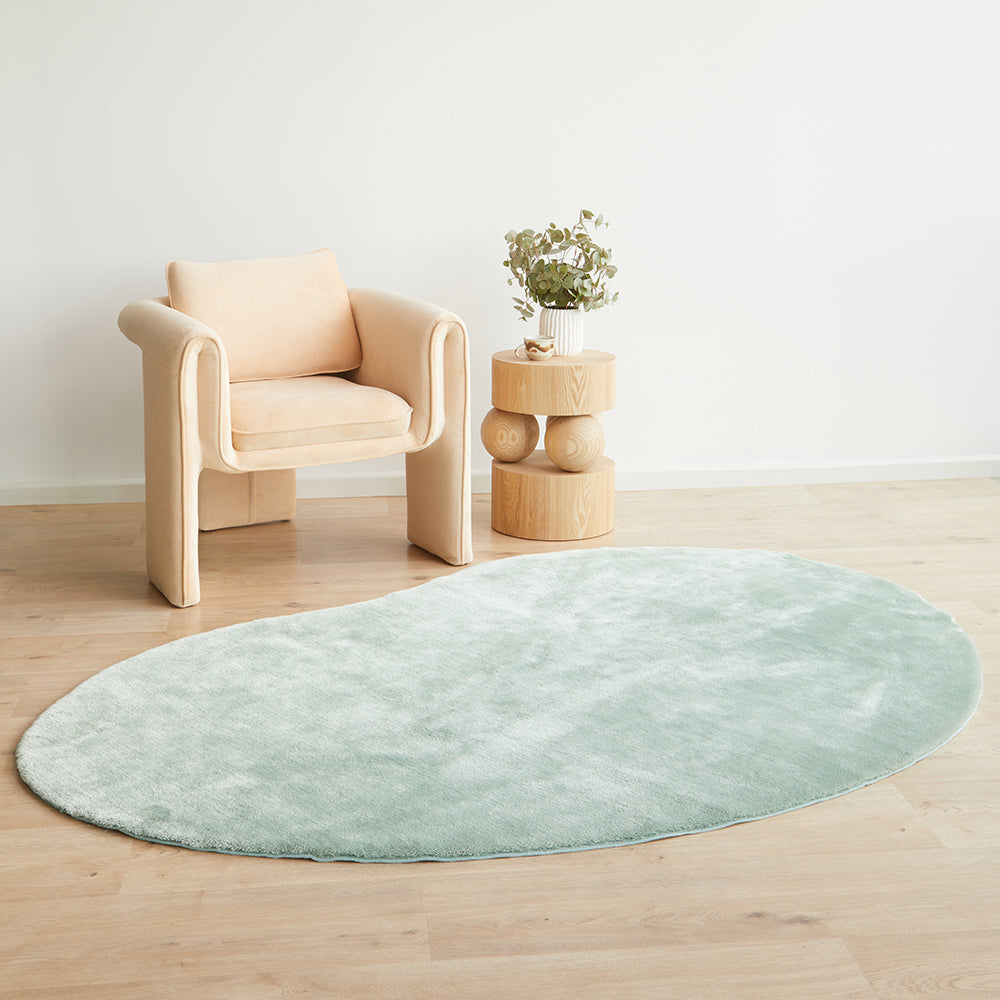 Oval pale green soft rug with plush texture on light wood floor.