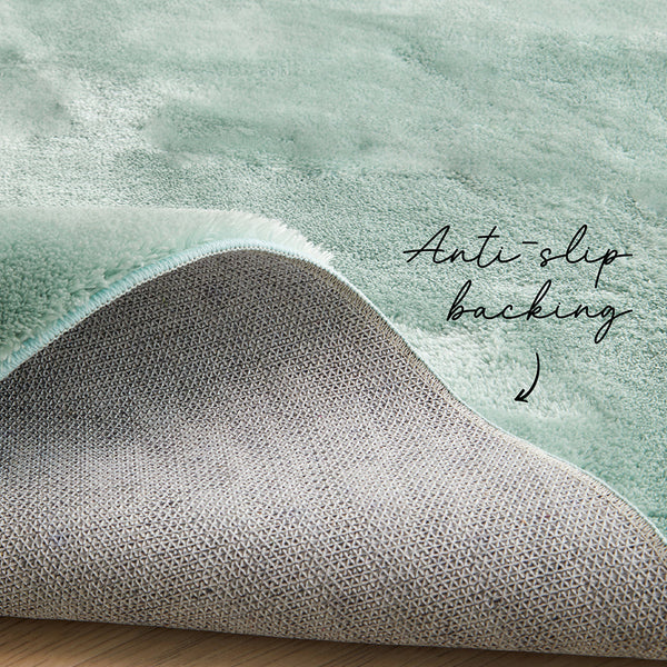 Pale green soft polyester rug corner turned up showing gray anti-slip backing and plush texture.